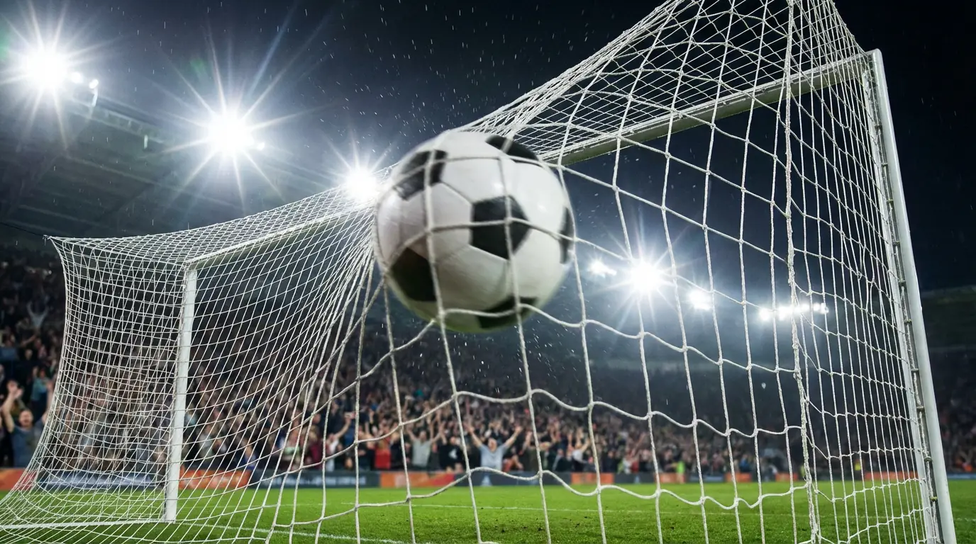 Football flying into the top corner of the goal with the net bulging under floodlights